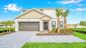 A modern two-story house with a garage, a well-maintained lawn, and a palm tree. - Upstay: Resort Villa w Pool & Cinema near Disney (Kissimmee)