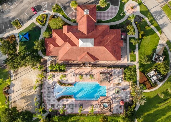 Vista aérea de un hotel con piscina, una zona cubierta con asientos y un estacionamiento.