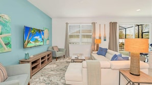 A living room with a sofa, TV, and a view of the outdoors. - Upstay: Resort Villa w Pool & Cinema near Disney (Kissimmee)