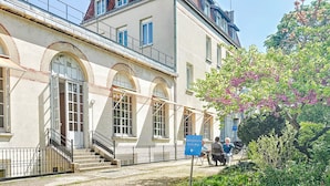 A building with a staircase leading to a balcony, a sign indicating 'Hôtelgehem' and 'Enclos Rey', and a tree with pink flowers. -  Hôtellerie de L'enclos Rey (Paris)