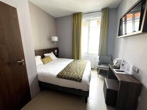 Quarto de hotel com cama, escrivaninha, cadeira e janela com cortinas.