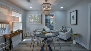 A modern dining area with a round table, clear chairs, and a chandelier.