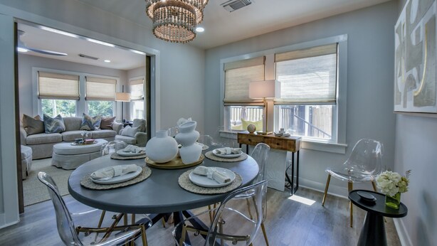 A modern dining area with a round table set for four, clear chairs, and a chandelier.