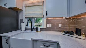 A modern kitchen with a large sink, white cabinets, and a window with a view of the outdoors.