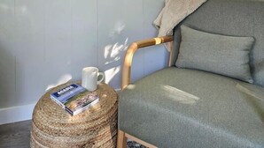 Een gezellige kamer met een grijze bank, een rond geweven poef en een poster van Acadia National Park.