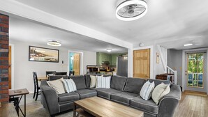 Een woonkamer met een hoekbank, een houten salontafel en een eethoek met een tafel en stoelen.
