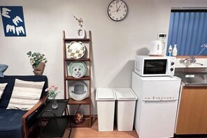 A compact living space with a sofa, a small table with a vase, a wall clock, a microwave, and a refrigerator. - Tabitime Oimasato Kiki 7min to Namba / 2min to Station /70 sqm house (Osaka)