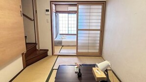 A traditional Japanese room with tatami flooring, a sliding door leading to a bed, and a small table with a vase and a telephone. - Tabitime Oimasato Kiki 7min to Namba / 2min to Station /70 sqm house (Osaka)