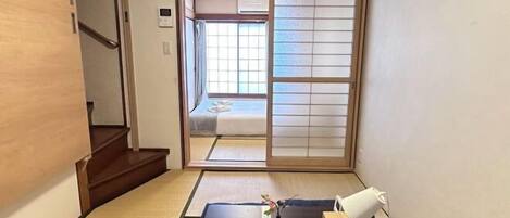 A traditional Japanese room with tatami flooring, a sliding door leading to a bed, and a small table with a vase and a telephone.