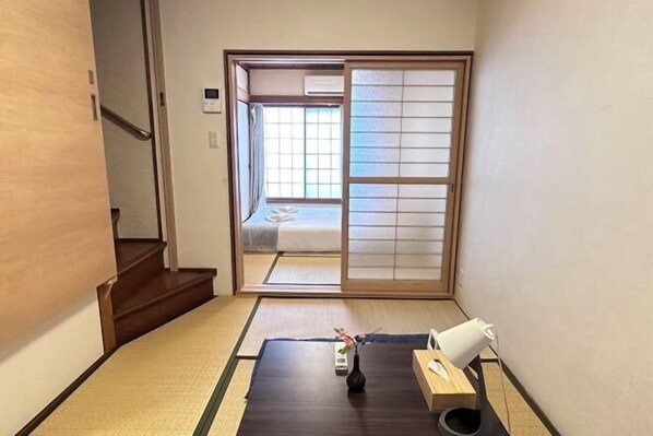 A traditional Japanese room with tatami flooring, a sliding door leading to a bed, and a small table with a vase and a telephone. - Tabitime Oimasato Kiki 7min to Namba / 2min to Station /70 sqm house (Osaka)