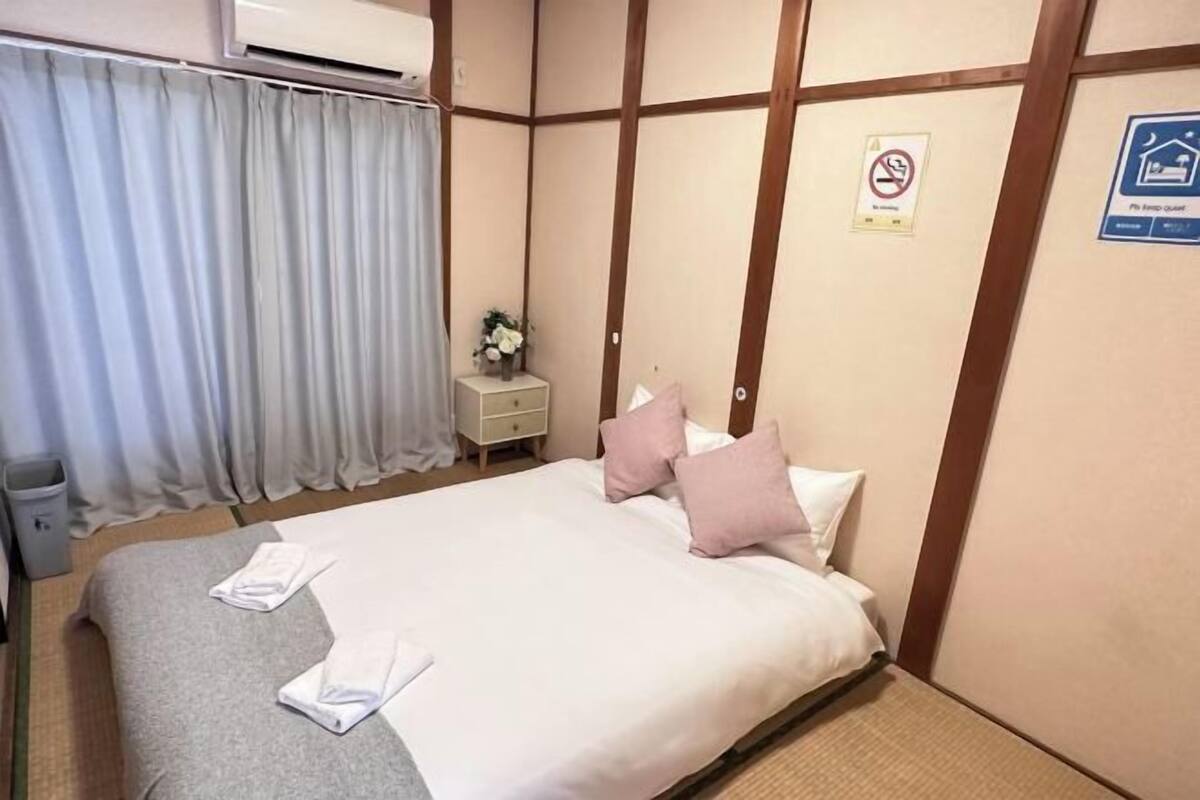 Ein Hotelzimmer mit Bett, Nachttisch, Mülleimer, einem Fenster mit Vorhängen und einem Schild mit der Aufschrift Rauchverbot.