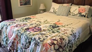 A neatly made bed with floral bedding, a wooden headboard, a bedside lamp, and a framed artwork on the wall.