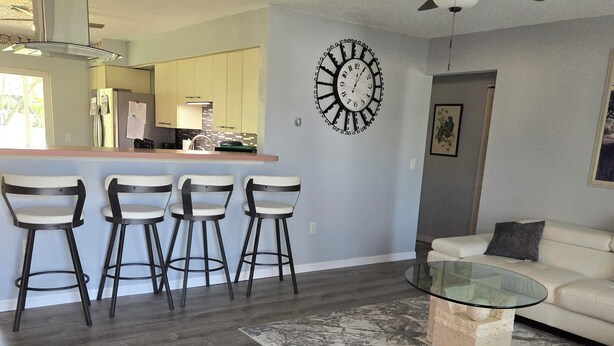 A modern living room with a glass coffee table, a sofa, and a kitchen area with a bar.