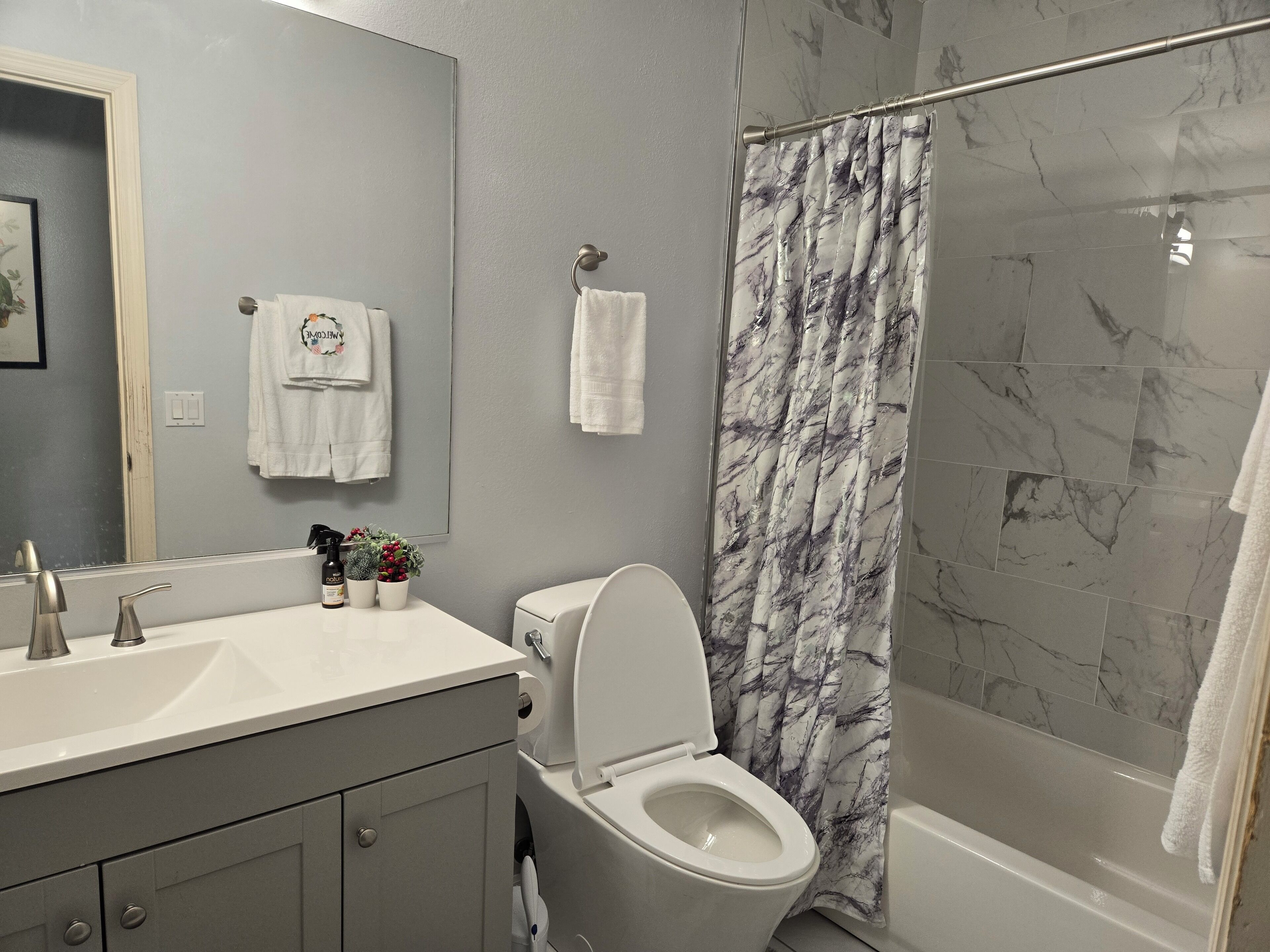 Een badkamer met een wit toilet, een wastafel met spiegel en een douche met een gordijn met marmerprint.
