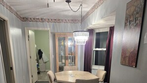 A dining room with a wooden table and chairs, a chandelier, and a cabinet with glass doors.