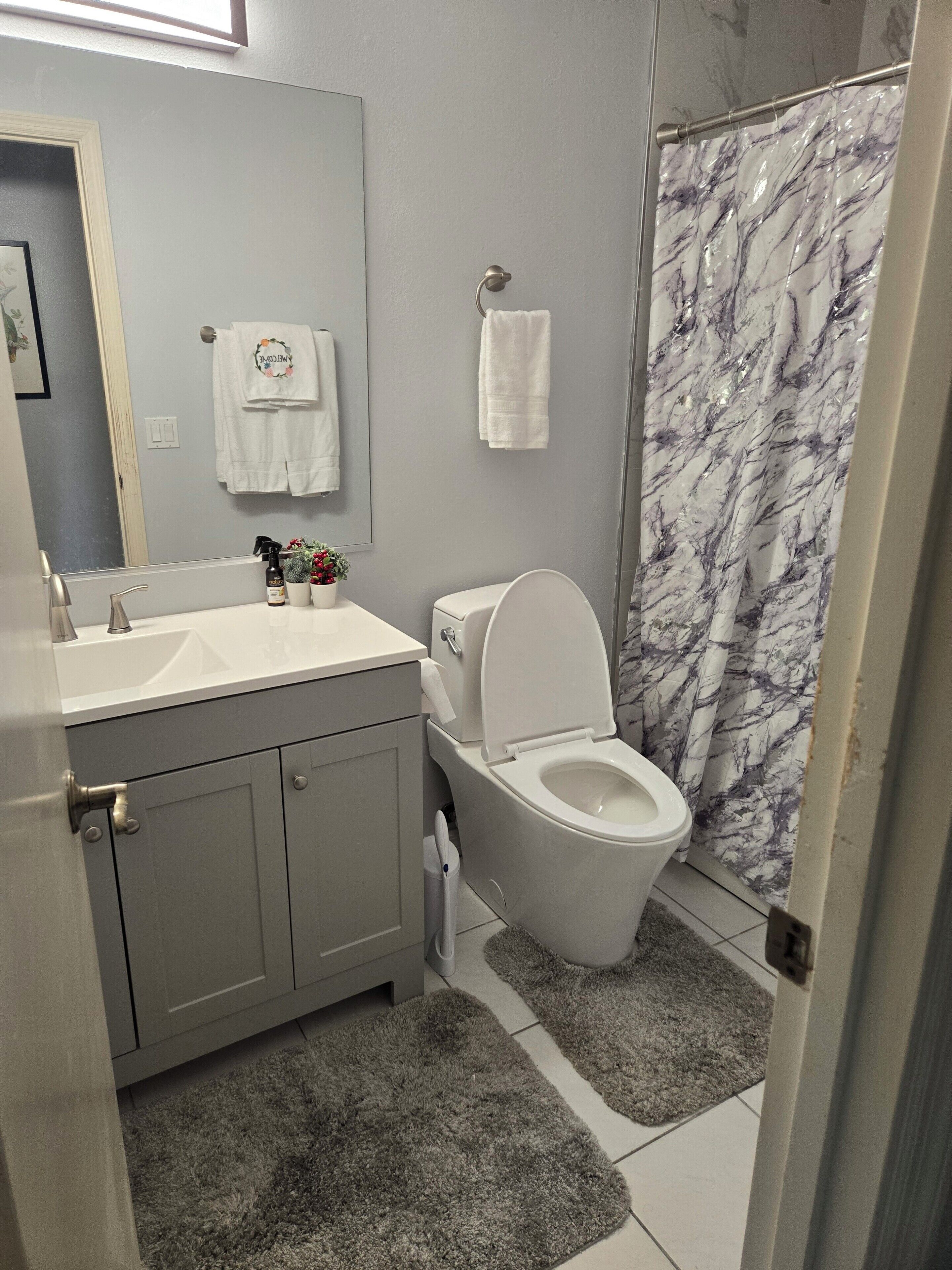 A bathroom with a toilet, sink, and mirror. There is a shower curtain with a marble pattern.