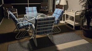 A living room with a glass-top table, striped chairs, a ceiling fan, and a potted plant.