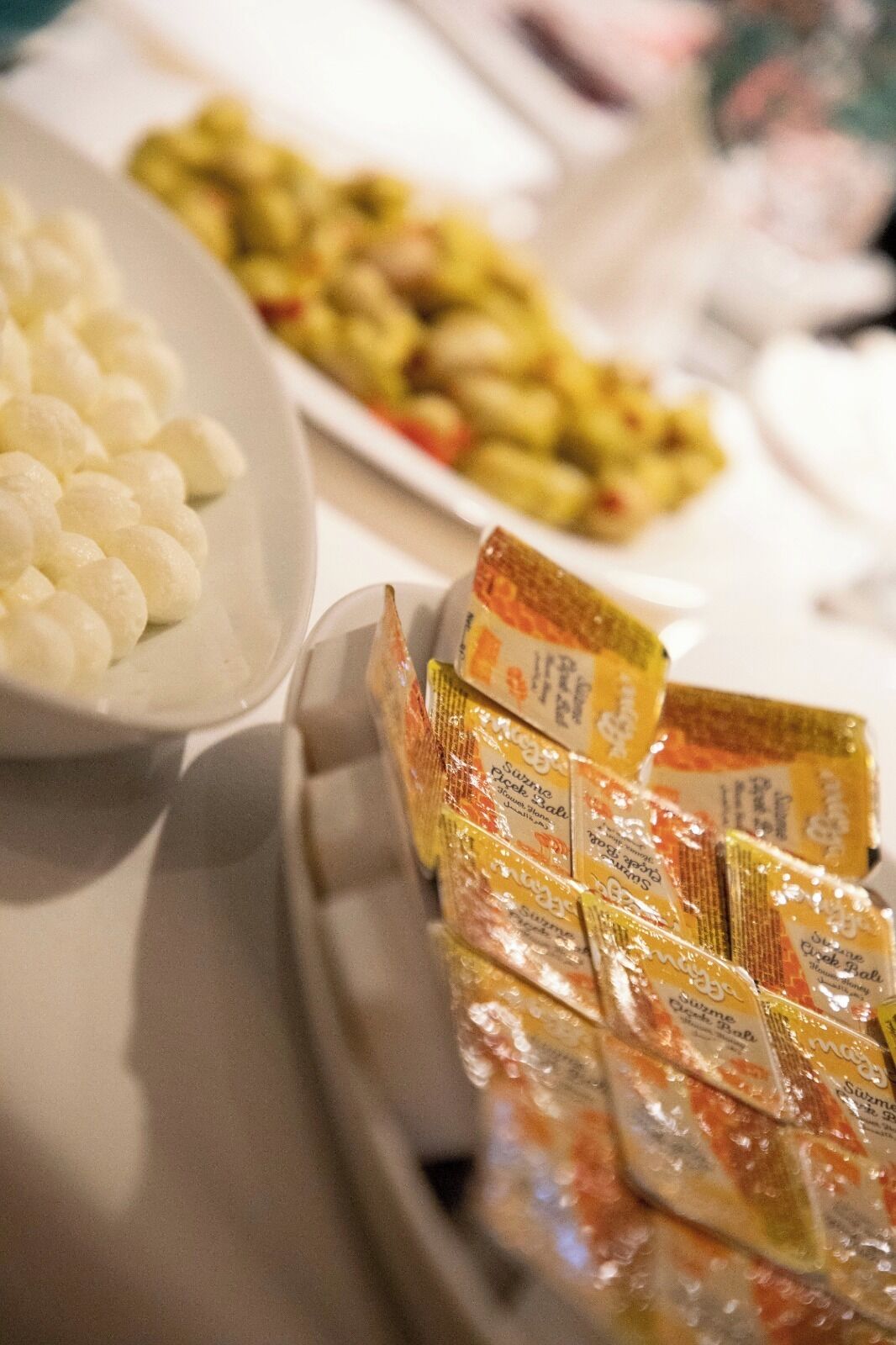 A table with various food items, including a plate of white round objects, a dish with mixed vegetables, and several packages of snacks.