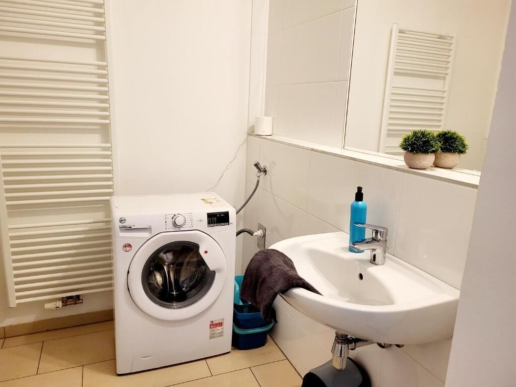 A compact bathroom with a washing machine, a sink, and a mirror.