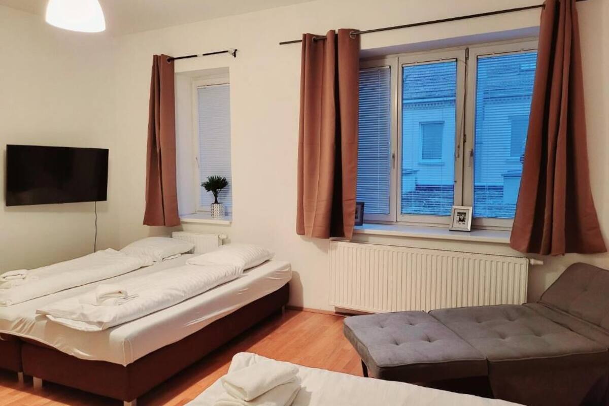 A room with two beds, a sofa, a TV, and a window with curtains.