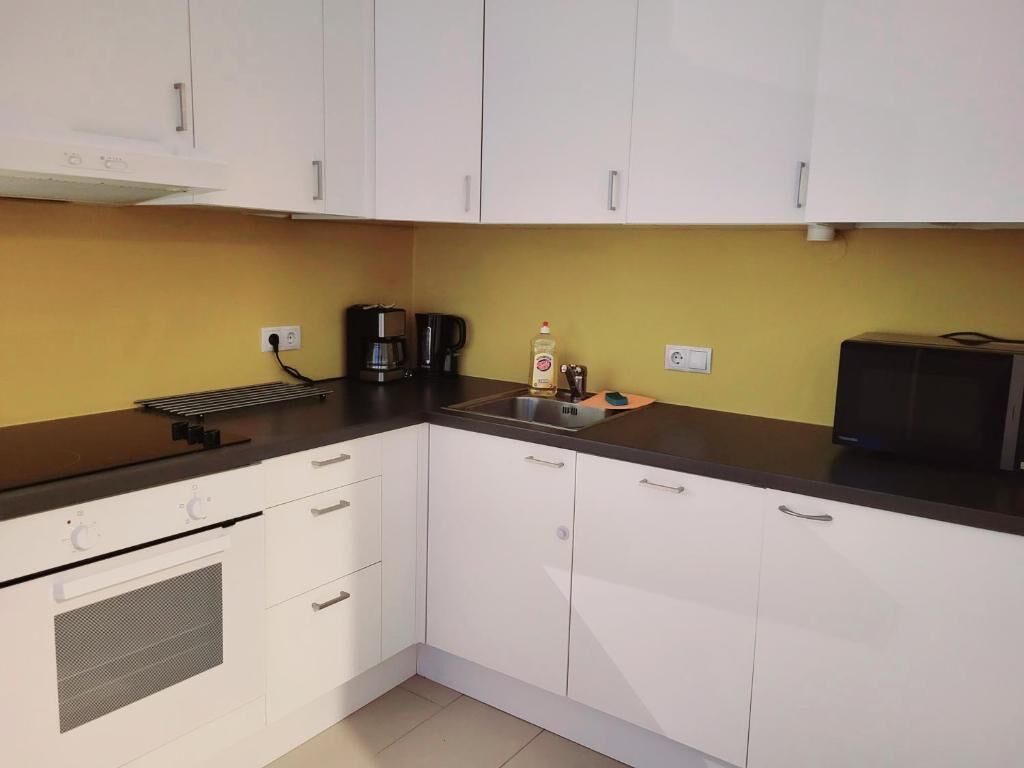 Cozinha compacta com armários brancos, bancada preta, cafeteira e torradeira.