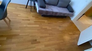A room with a wooden floor, a grey sofa, a black chair, and a white cabinet. - Floridsdorfer Apartment (Vienna)