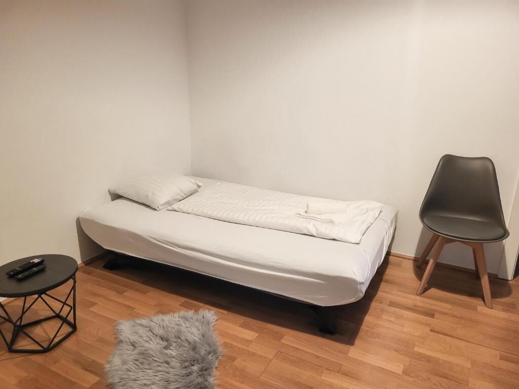 A small, neatly arranged room with a single bed, a chair, a small round table, and a fluffy rug.