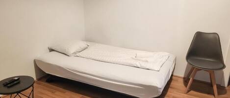 A small, neatly arranged room with a single bed, a chair, a small round table, and a fluffy rug.