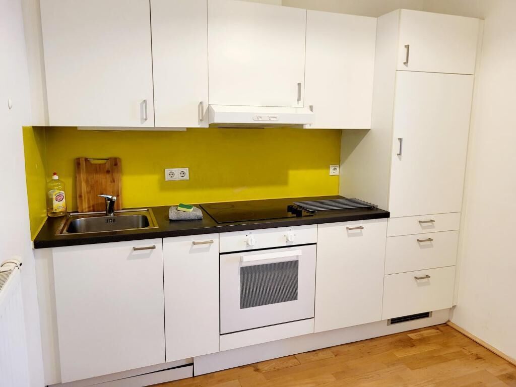 Una cucina con mobili bianchi, un piano di lavoro nero, un lavandino, un fornello e un backsplash giallo.