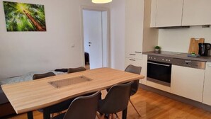 A modern kitchen with white cabinets, a wooden dining table, and black chairs. - Floridsdorfer Apartment (Vienna)