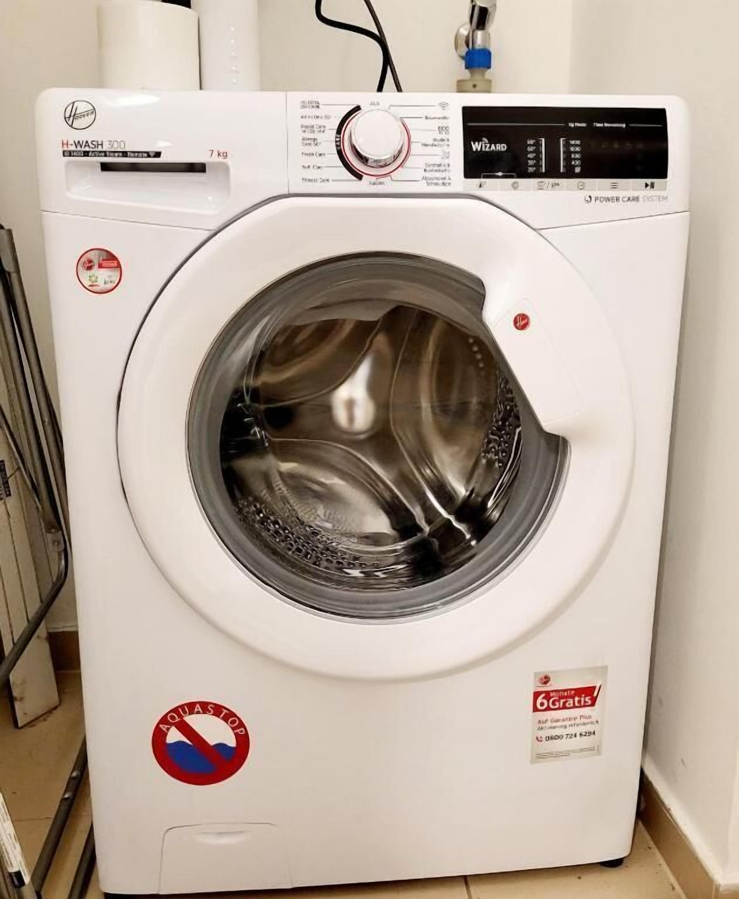 A front-loading washing machine with a digital display, a 7 kg capacity, and a "6Gratis" promotional sticker.