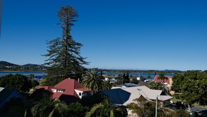 A coastal residential area with houses, a prominent tall tree, and a view of the sea and distant mountains. - Tranquil, Stylish, Retreat - 3 Bedrooms (Tuncurry)