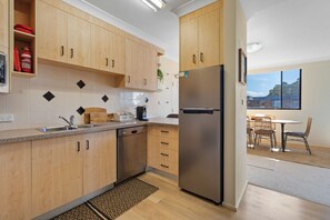 A modern kitchen with wooden cabinets, a stainless steel refrigerator, and a dining area with a table and chairs.