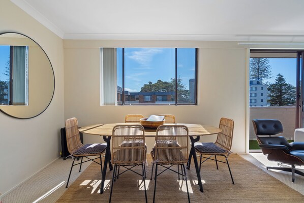 A room with a dining table, four chairs, a large mirror, and a view of buildings through large windows.