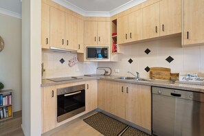 A modern kitchen with wooden cabinets, a built-in microwave, a coffee bar, and a Bosch dishwasher.