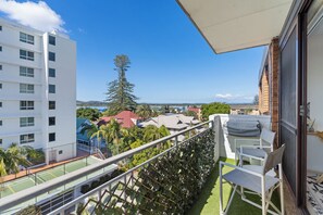A balcony with a view of a tennis court, a tall tree, and buildings in the background.