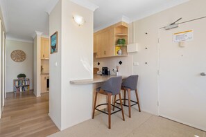 A modern kitchen with wooden cabinets, a built-in island with bar stools, and a visible clock.