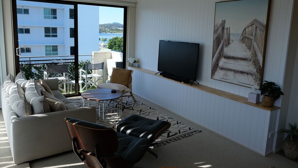 A living room with a sofa, a coffee table, a TV, and a painting. - Tranquil, Stylish, Retreat - 3 Bedrooms (Tuncurry)