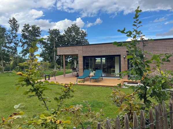 A modern house with a deck, outdoor seating, and a garden.