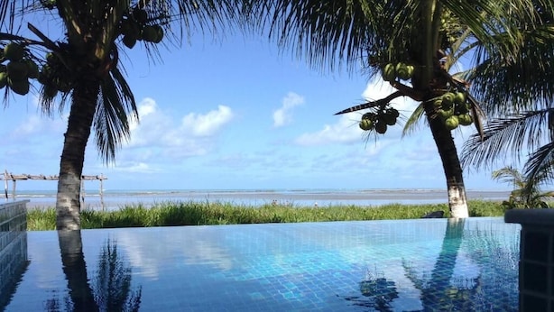 Uma piscina infinita azul límpida com vista para o oceano e palmeiras.