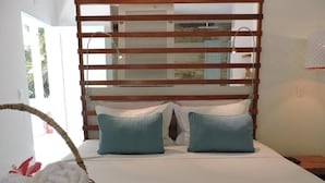 Quarto com cama, cabeceira de madeira, cesta de toalhas e colcha azul-esverdeada.