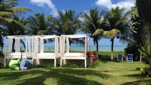 Um cenário à beira-mar com um gazebo branco, duas cadeiras de descanso e uma pequena área de piscina.