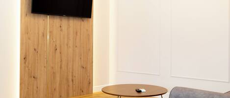 A modern living room with a flat-screen TV mounted on a wooden panel wall, a round wooden coffee table, and a gray sofa.