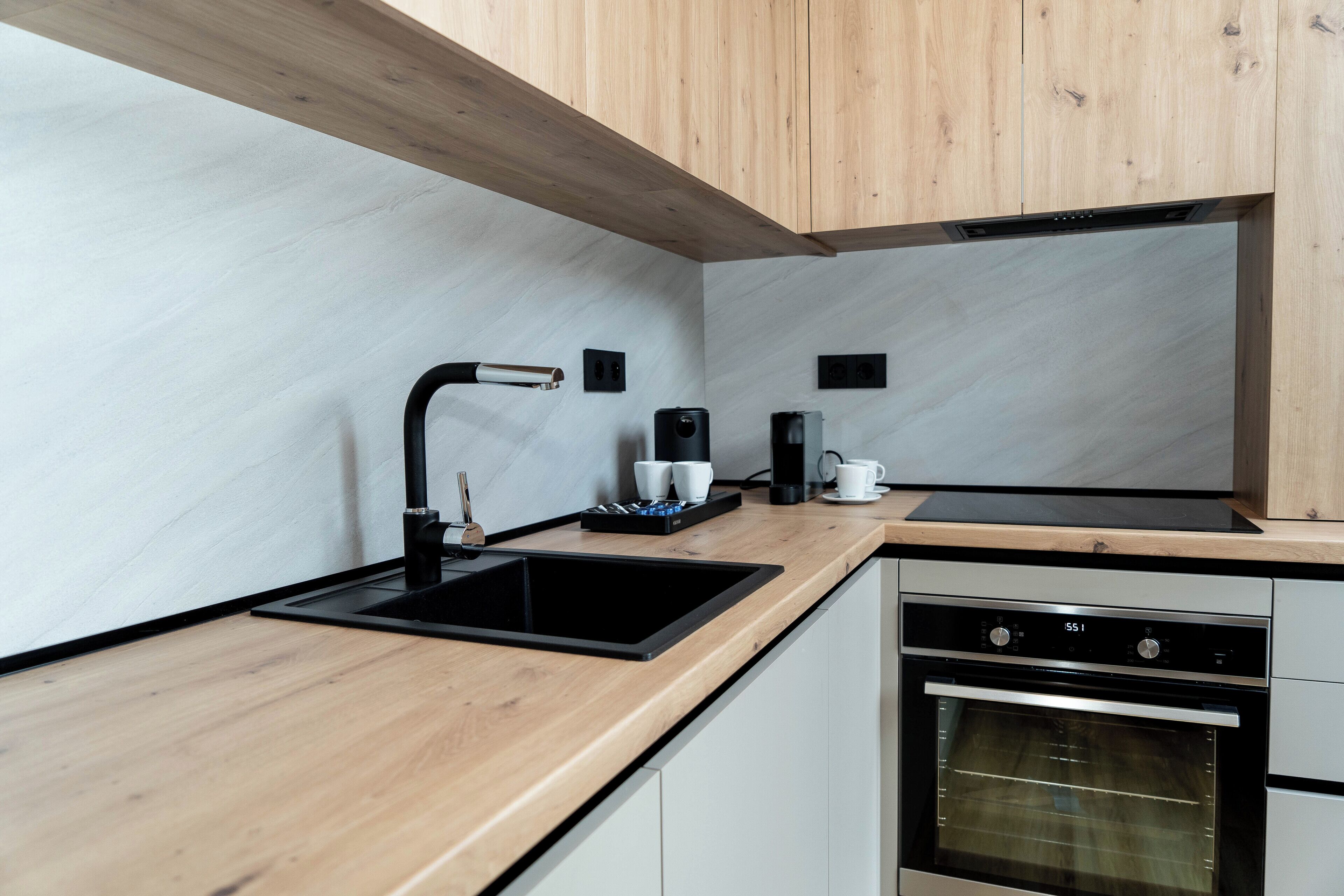 A modern kitchen with a black sink, wooden countertop, and built-in oven.