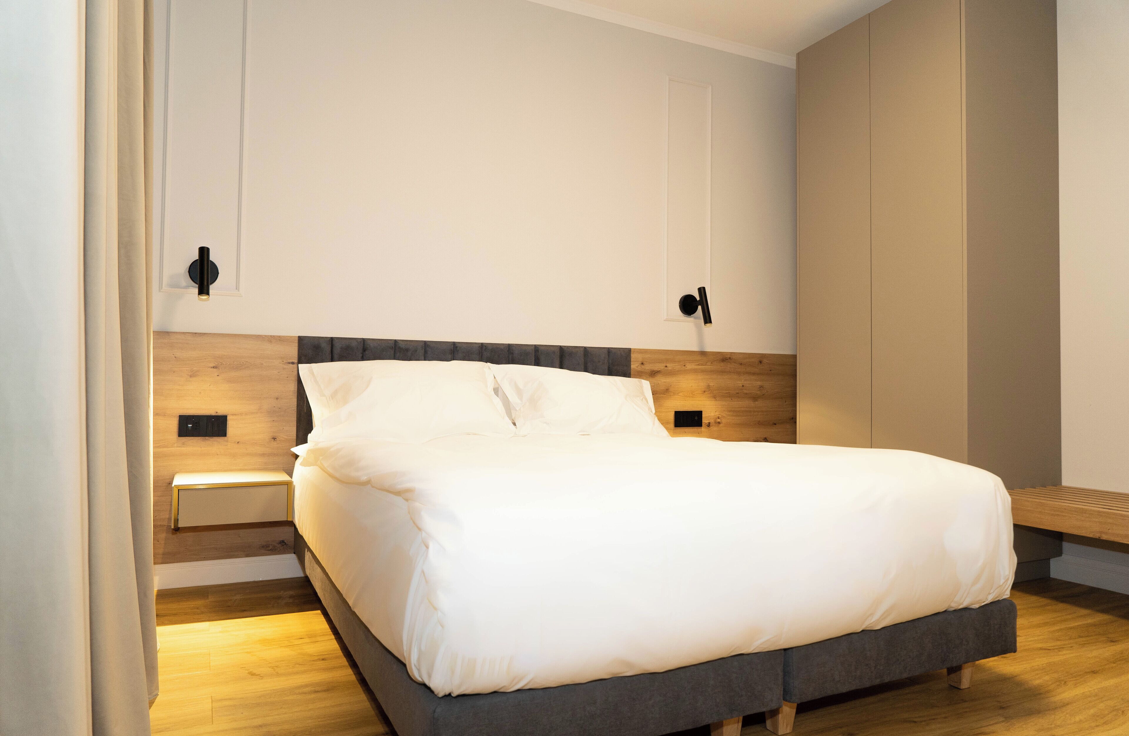Quarto moderno com cabeceira de madeira, um banco de madeira e uma mesa de cabeceira.