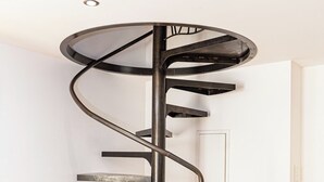 A spiral staircase with a modern design, made of metal and glass, in a room with wooden flooring and white walls. - Charming house in the heart of the village La nuit étoilée (Saint-Martin-de-Crau)