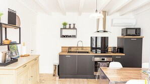 A modern kitchen with a wooden countertop, black cabinets, a sink, a microwave, and a stove. There is a small shelf with decorative items and a hanging light fixture. - Charming  Townhouse Mon voisin Van Gogh (Arles)