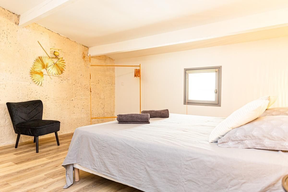 A bedroom with a bed, a chair, a window, and a wall decoration.
