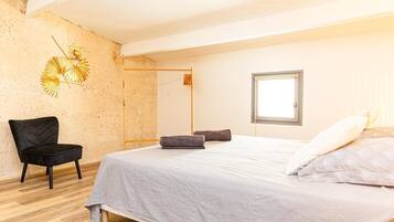 A bedroom with a bed, a chair, a window, and a wall decoration.