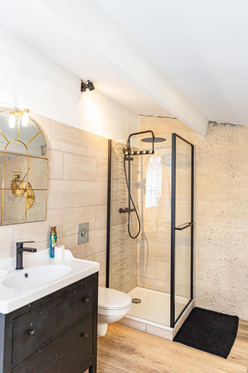 A modern bathroom with a glass-enclosed shower, a white sink, and a large mirror with a gold frame.
